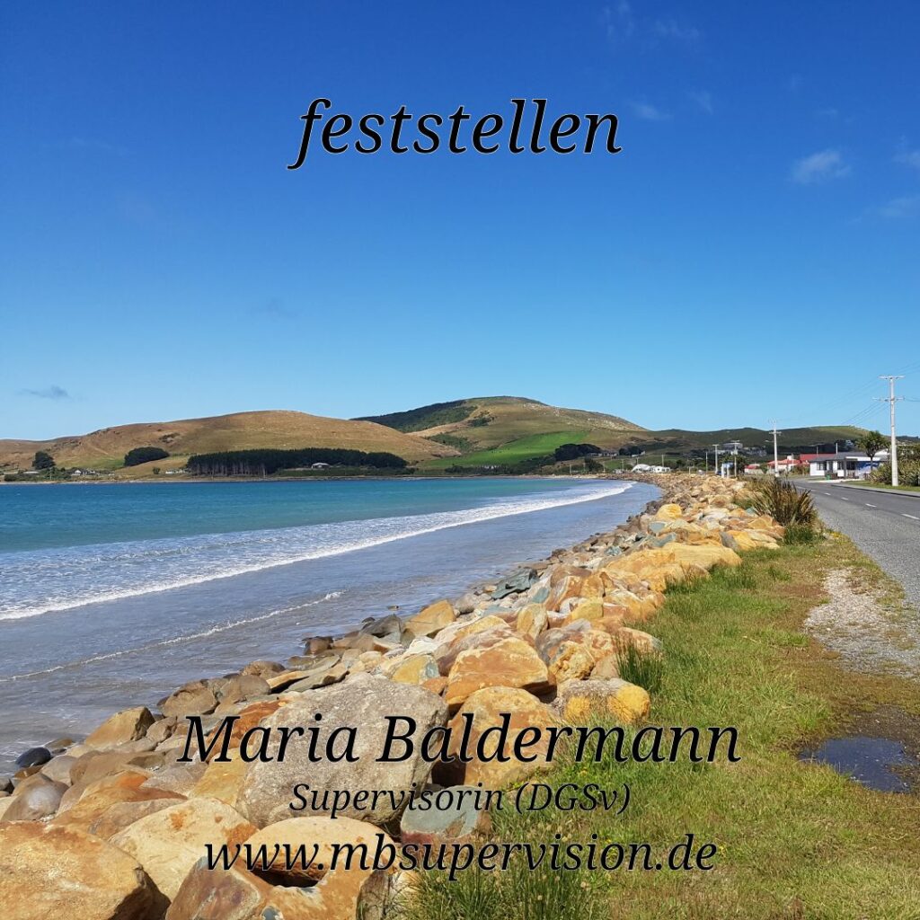 Küstenlandschaft mit einem Steinwall, der das Ufer von einer schmalen Straße trennt. Im Hintergrund sanfte, grüne Hügel unter blauem Himmel. Im Vordergrund ist der Strand mit ruhigem Wasser zu sehen. Oben steht das Wort 'feststellen'. Unten im Bild sind der Name 'Maria Baldermann', die Berufsbezeichnung 'Supervisorin (DGSV)' und die Internetadresse 'www.mbsupervision.de' zu lesen.