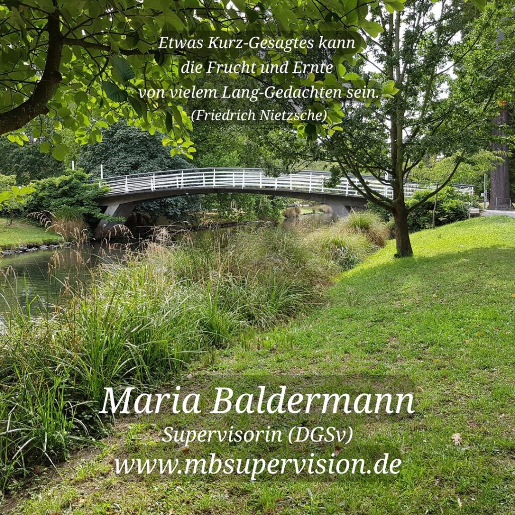 Grüne Parklandschaft mit einer Bogenbrücke mit weißem Geländer über einen Bach und Bäumen im Hintergrund. Im oberen Bereich steht ein Zitat: 'Etwas Kurz-Gesagtes kann die Frucht und Ernte von vielem Lang-Gedachten sein. (Friedrich Nietzsche)' Unten im Bild sind der Name 'Maria Baldermann', die Berufsbezeichnung 'Supervisorin (DGSV)' und die Internetadresse 'www.mbsupervision.de' zu lesen.