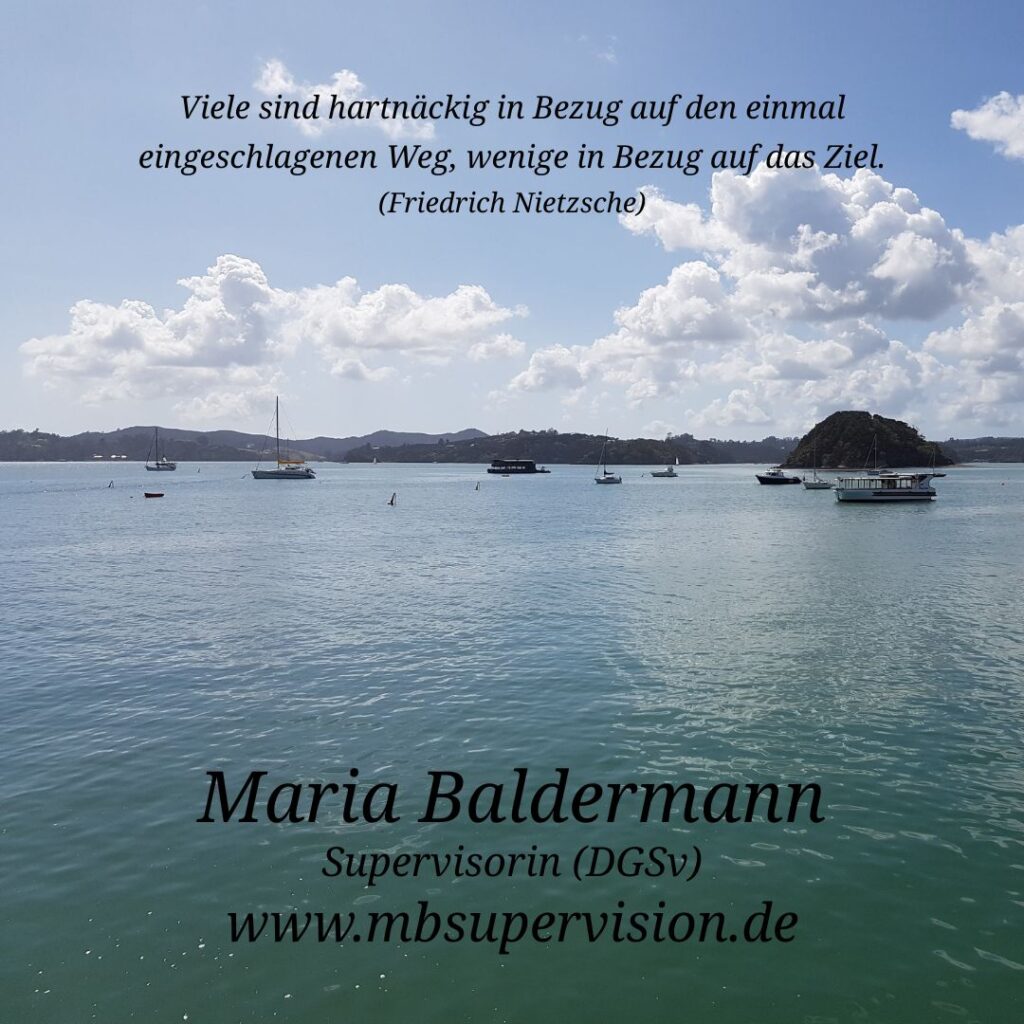 Im Vordergrund erstreckt sich eine ruhige Wasserfläche mit mehreren Segelbooten und kleinen Schiffen. Im Hintergrund sind bewaldete Hügel und eine kleine Insel zu sehen. Der Himmel ist leicht bewölkt. Im oberen Bereich steht ein Zitat: 'Viele sind hartnäckig in Bezug auf den einmal eingeschlagenen Weg, wenige in Bezug auf das Ziel. (Friedrich Nietzsche)'. Unten im Bild sind der Name 'Maria Baldermann', die Berufsbezeichnung 'Supervisorin (DGSV)' und die Internetadresse 'www.mbsupervision.de' zu lesen.